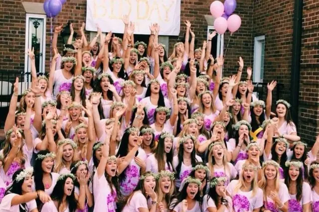 Archive photograph of women in pink gathered on outdoor steps beneath balloons.