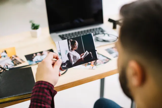 Stock photograph of someone holding a photographic print beside a computer.