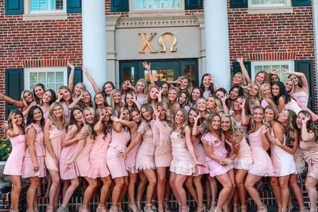 Archive group photograph of women wearing pink outside a brick sorority house.
