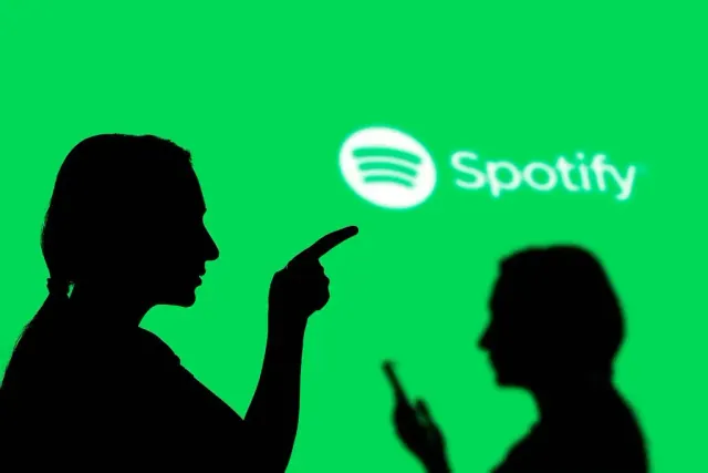 The silhouettes of two people in front of a bright green background with a Spotify logo