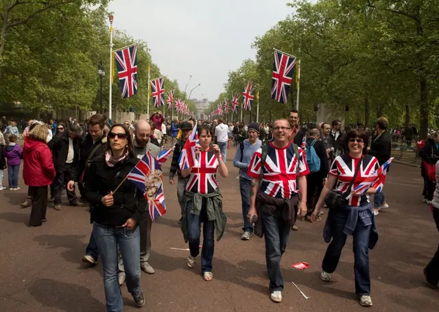 Archive photograph of people carrying British flags on a tree-lined road.