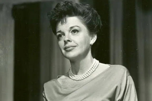 Black-and-white archive portrait of Judy Garland wearing a light dress and necklace.