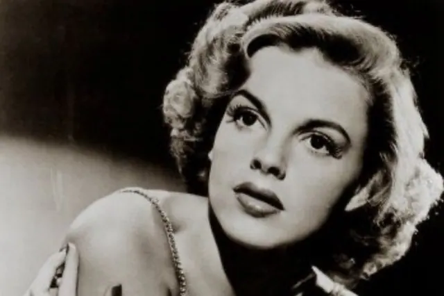 Black-and-white archive portrait of Judy Garland resting her chin on her hand.