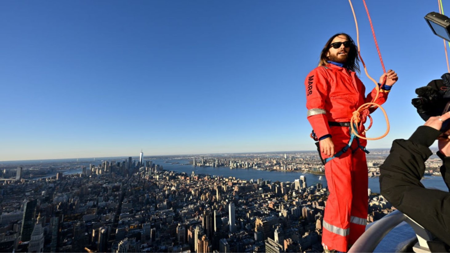 Jared Leto wearing climbing gear high above New York City