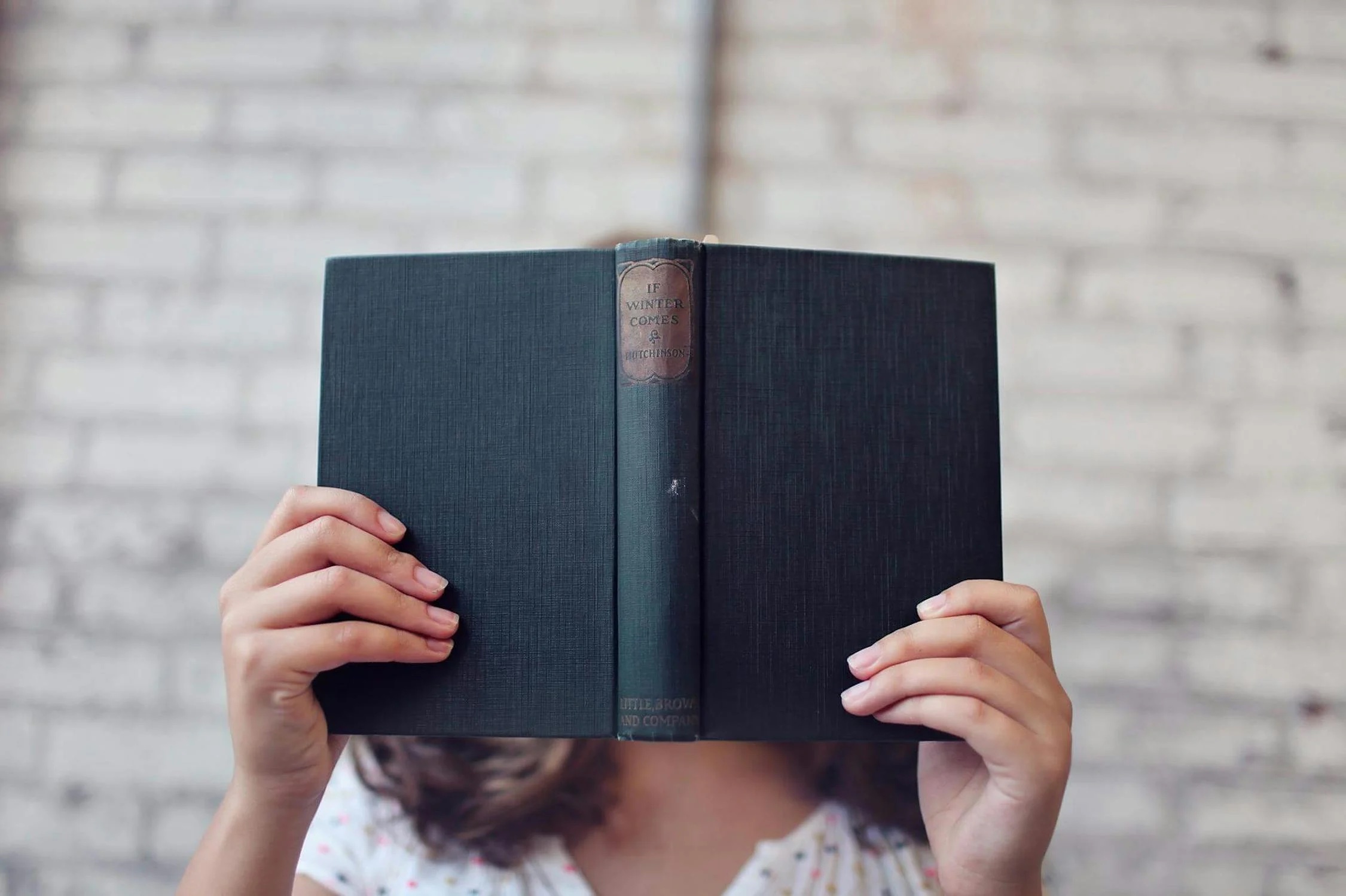 A person holding a book before their face; illustrative photograph.