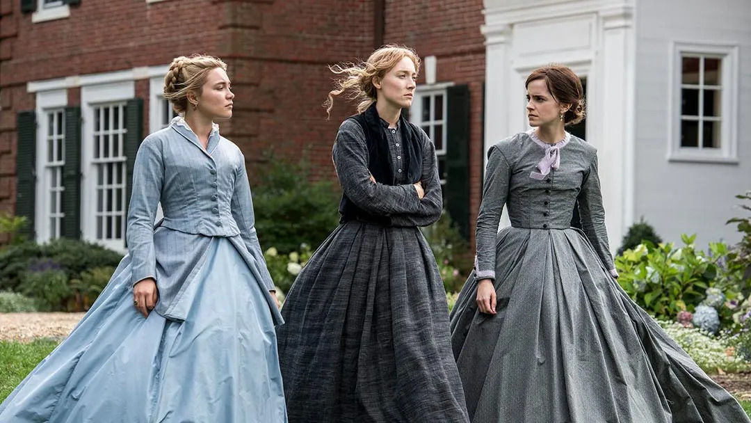 Three performers in period dresses beside a brick building